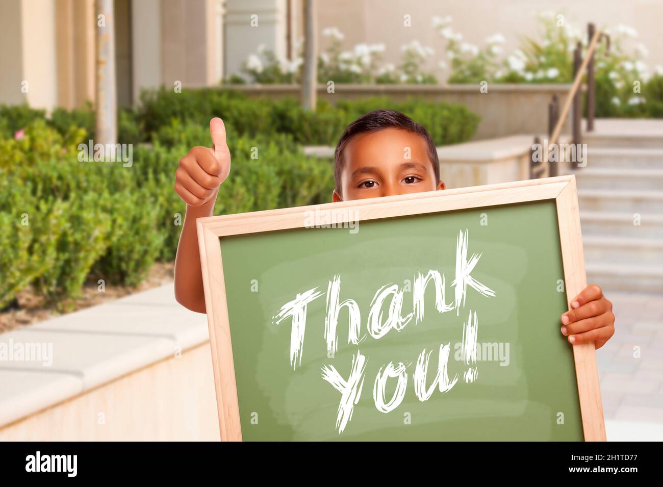 Happy Hispanic Boy Ding Thumbs Up holding Thank You Chalk Board à l'extérieur sur le campus de l'école. Banque D'Images