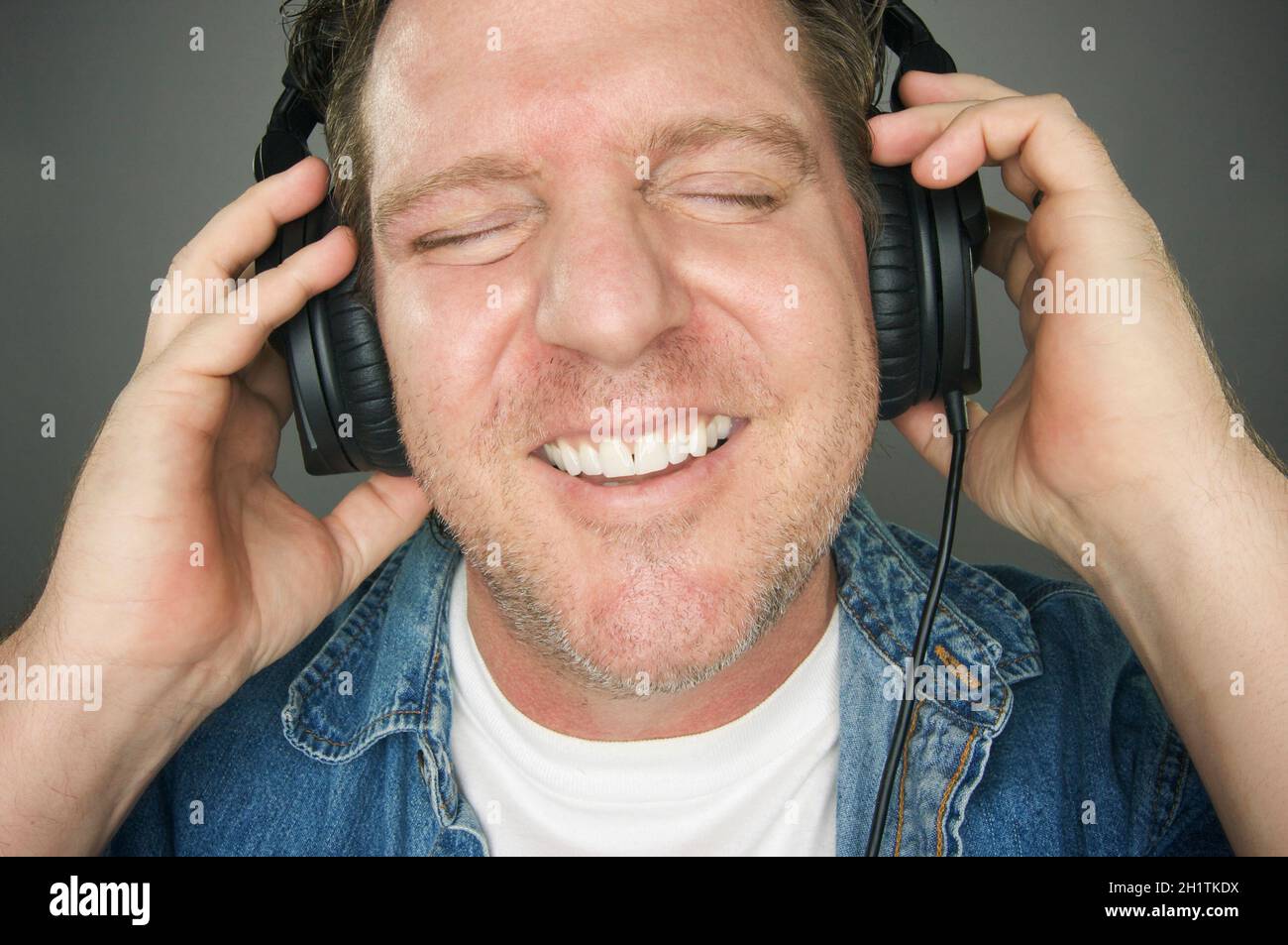 L'homme avec les yeux fermés portant des écouteurs appréciant sa musique  sur un fond gris Photo Stock - Alamy