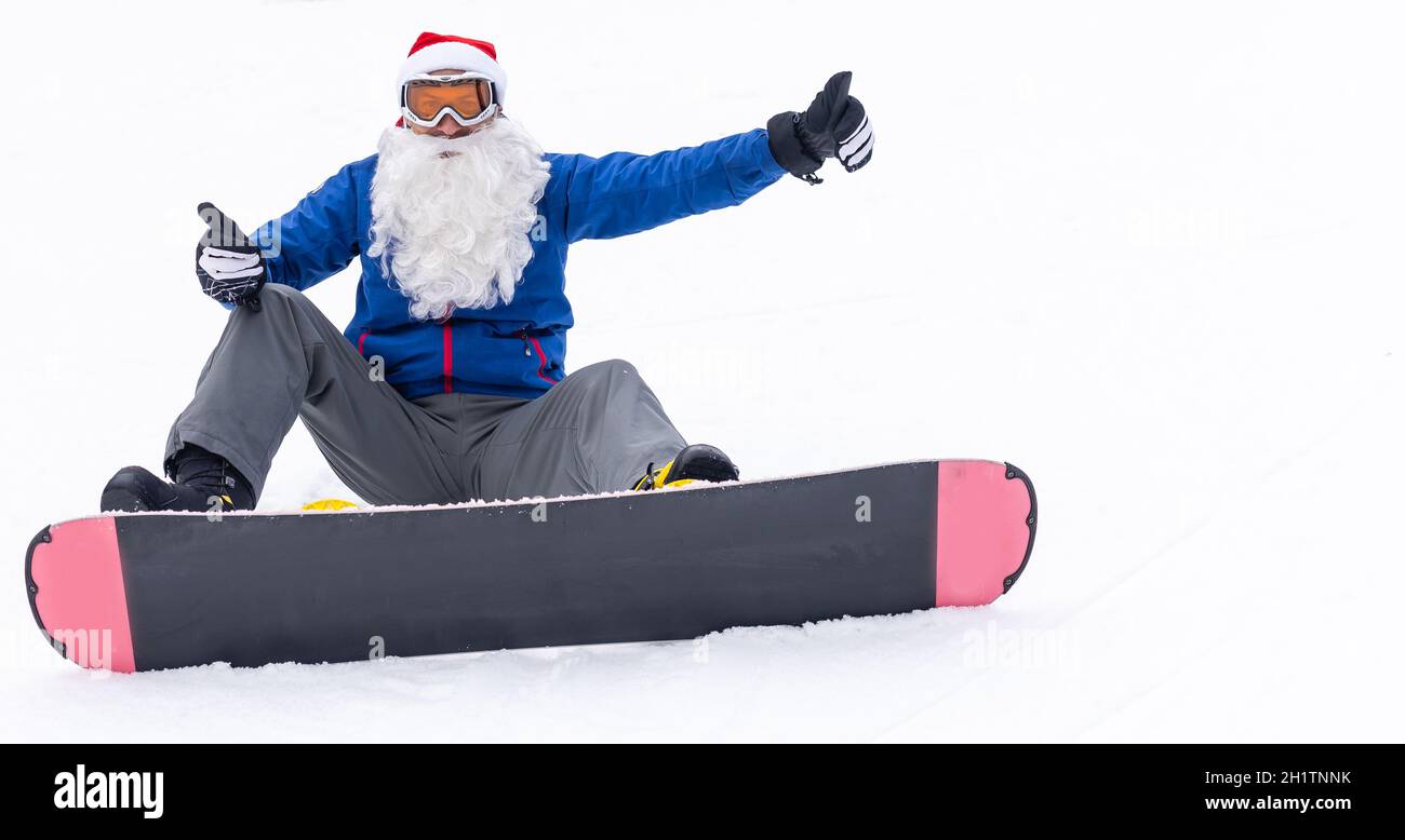 un homme dans un chapeau de père noël avec un snowboard dans une station de ski Banque D'Images