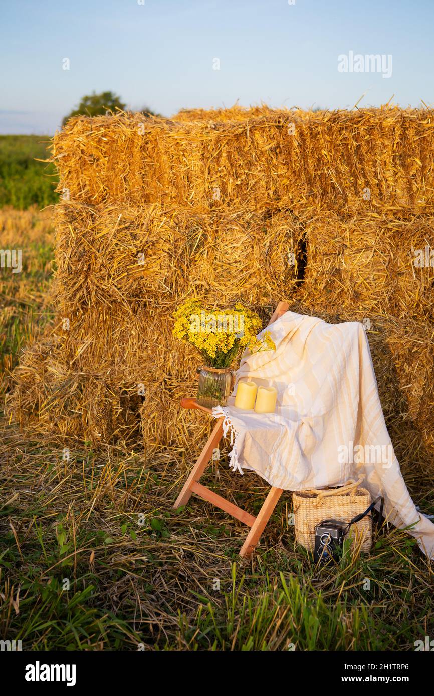 Pique-niquez dans le champ près des balles de paille. Le soleil couchant. Style rustique - chaise en bois, écossais, bouquet de fleurs, bougies Banque D'Images