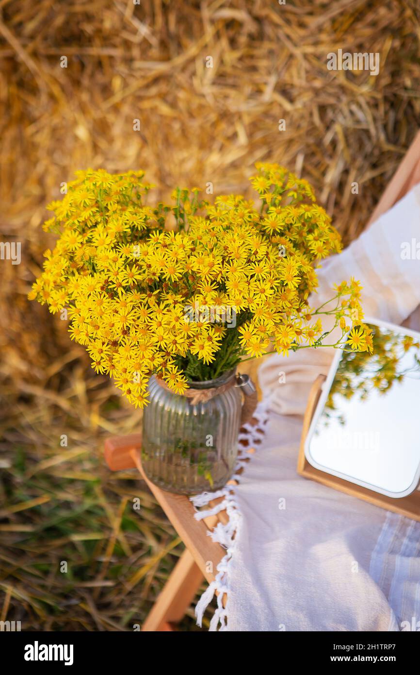 Pique-niquez dans le champ près des balles de paille. Le soleil couchant. Style rustique - chaise en bois, carreaux, bouquet de fleurs, miroir. Date romantique Banque D'Images