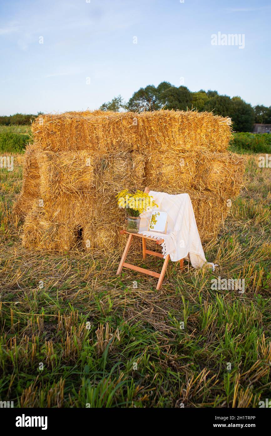 Pique-niquez dans le champ près des balles de paille. Le soleil couchant. Style rustique - chaise en bois, carreaux, bouquet de fleurs, miroir. Date romantique Banque D'Images
