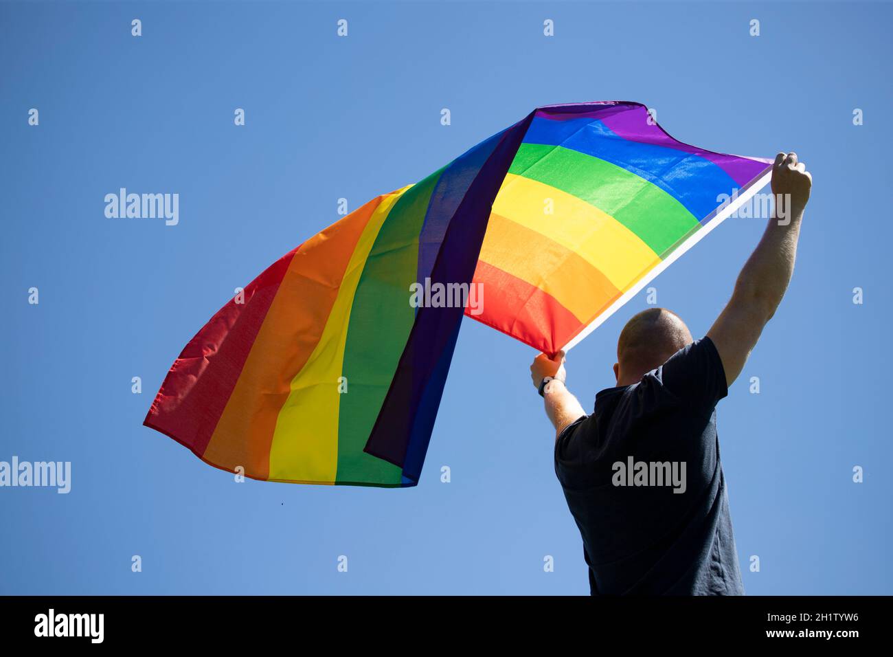 Homme tenant un drapeau arc-en-ciel gay sur bleu ciel d'été. Symbole bisexuel, gay, lesbien, transsexuel. Concept de bonheur, de liberté et d'amour pour le même sexe coupé Banque D'Images
