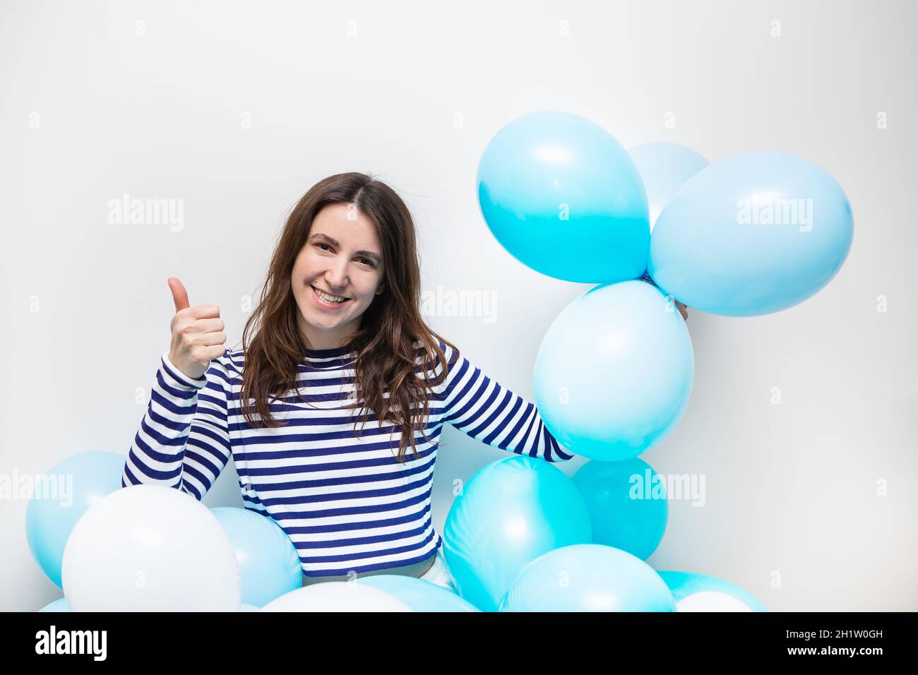 Une fille heureuse dans un chandail rayé sourit et tient des ballons bleus dans ses mains. Place pour une inscription, concept de vacances Banque D'Images