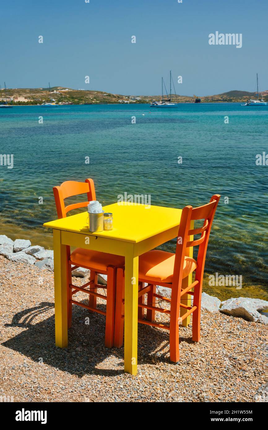 Restaurant café jaune table de café de rue avec chaises sur la plage dans la ville d'Adamantas sur l'île de Milos avec la mer Égée avec des bateaux et des yachts en arrière-plan Banque D'Images