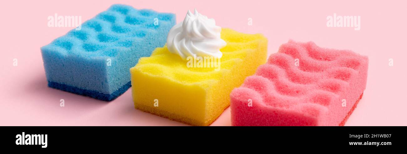 Éponges colorées pour laver la vaisselle avec mousse sur fond rose Banque D'Images