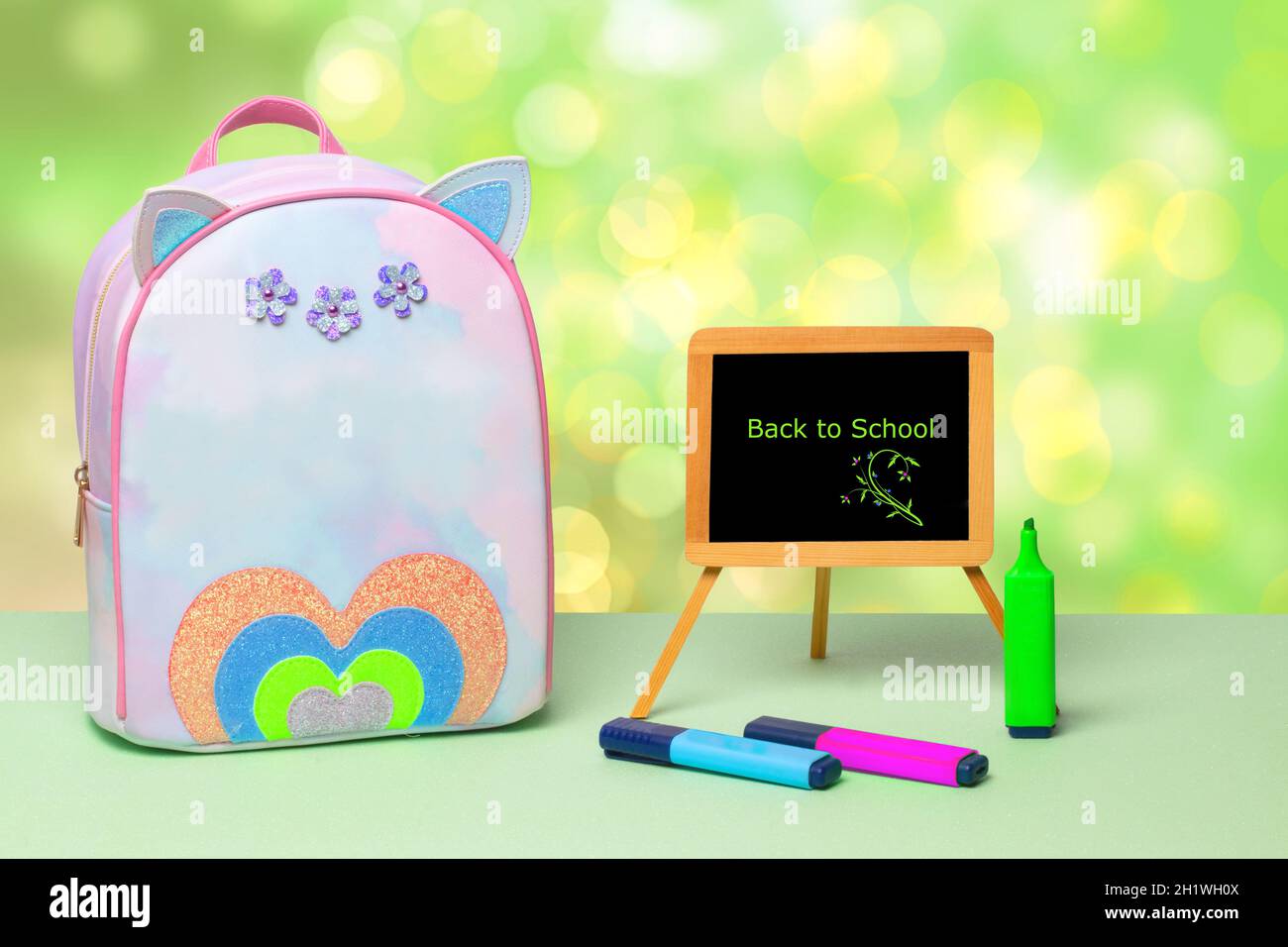 Le retour à l'école est écrit en lettres vertes sur un tableau noir, des crayons colorés et un sac à dos d'école coloré sur une table verte au-dessus d'un résumé Banque D'Images