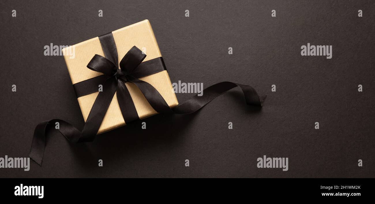 Black Friday sale concept, boîte cadeau papier kraft brun avec ruban noir noeud sur fond sombre, bannière, espace.Promotion vacances hiver de Banque D'Images