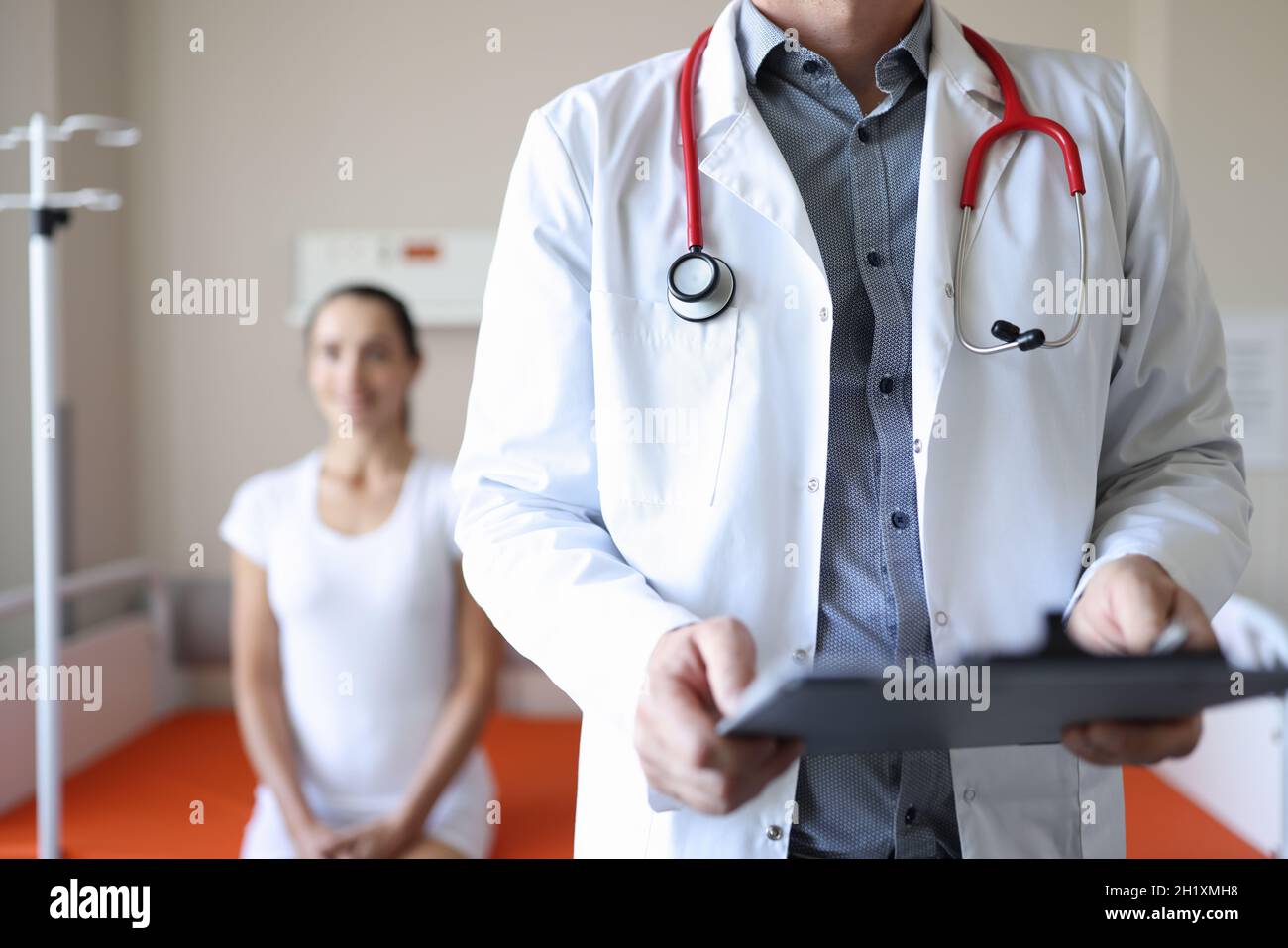 Le médecin tient la planchette à pince avec les documents médicaux en arrière-plan le patient est assis Banque D'Images
