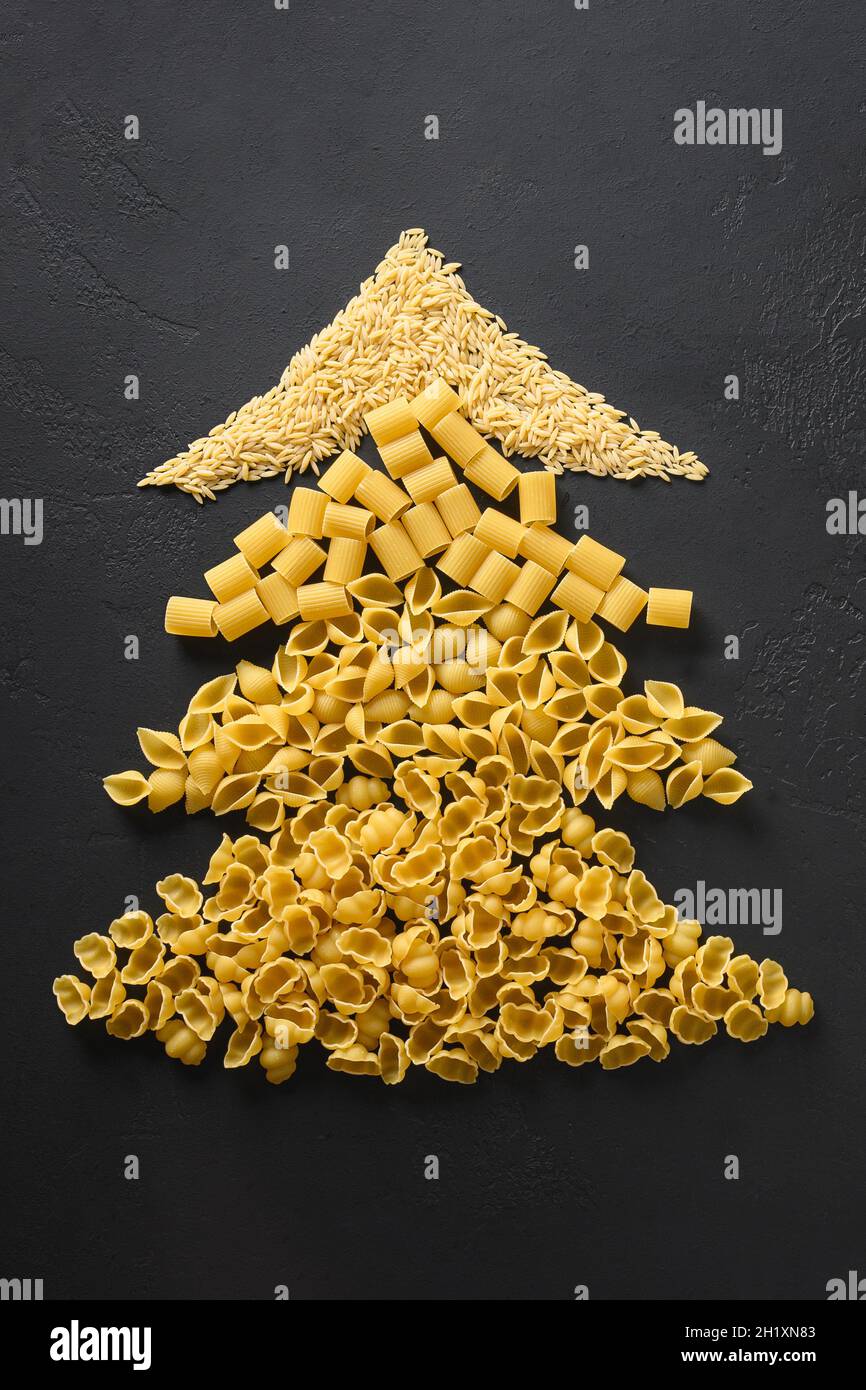 Arbre de Noël créatif alternatif de différentes pâtes sèches sur fond noir.Carte de vœux de Noël.Vue de dessus.Concept de vacances gastronomiques. Banque D'Images