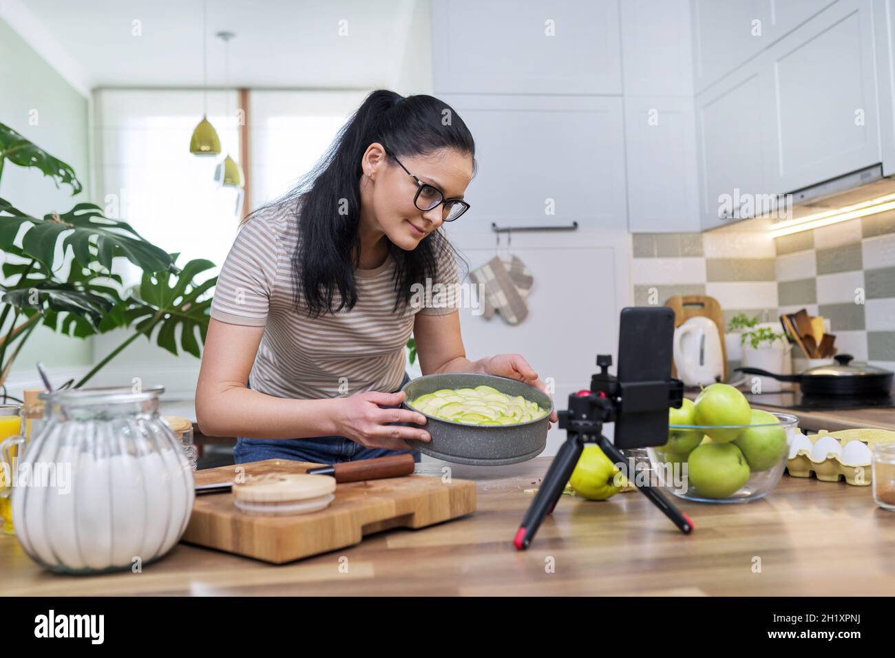Femme préparant une tarte aux pommes à la maison dans la cuisine, avec un smartphone en utilisant un appel vidéo Banque D'Images