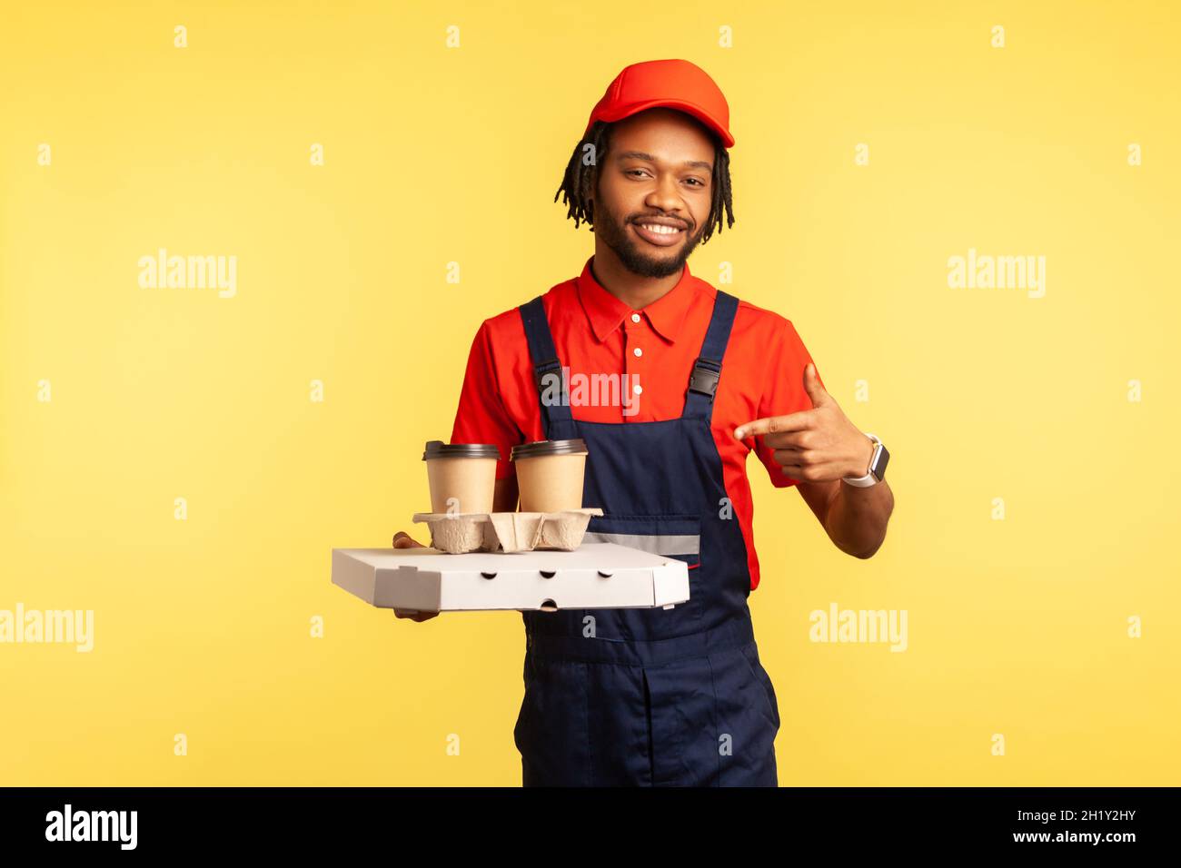 Service de livraison.Un messager optimiste dans des combinaisons bleues pointant vers le café et la boîte avec la restauration rapide, offrant des boissons dans des tasses jetables et de la pizza.Studio d'intérieur isolé sur fond jaune. Banque D'Images Service de livraison.Un messager optimiste dans des combinaisons bleues pointant vers le café et la boîte avec la restauration rapide, offrant des boissons dans des tasses jetables et de la pizza.Studio d'intérieur isolé sur fond jaune. Banque D'Images