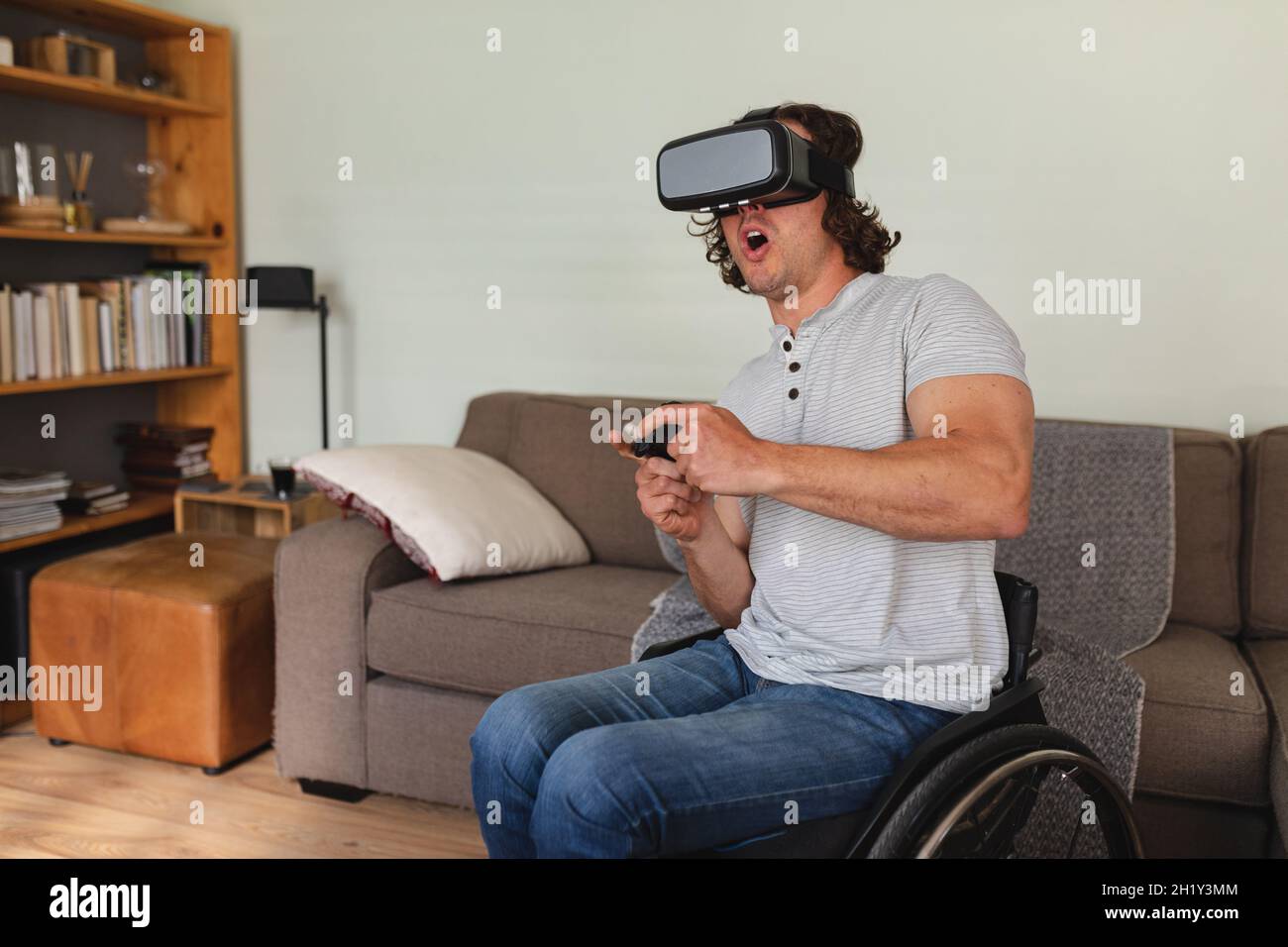 Homme cacaucasien handicapé assis sur un fauteuil roulant portant un casque vr et jouant à des jeux vidéo à la maison Banque D'Images