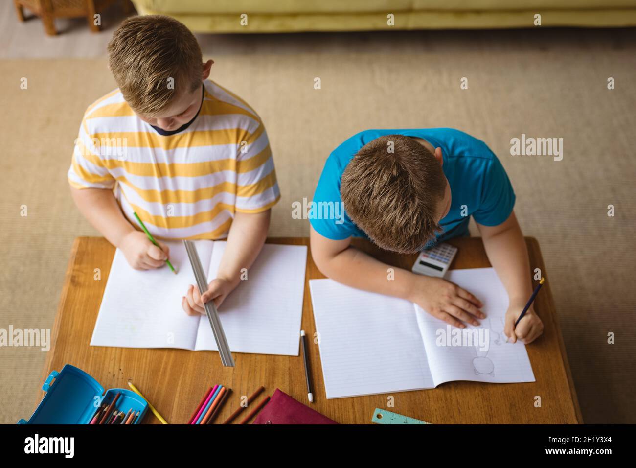 Vue en hauteur de deux garçons caucasiens qui dessinant dans leurs livres, assis dans le salon à la maison Banque D'Images