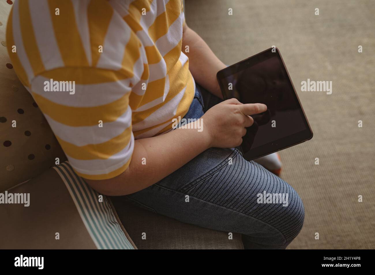 Section médiane d'un garçon caucasien utilisant une tablette numérique assis sur le canapé à la maison Banque D'Images