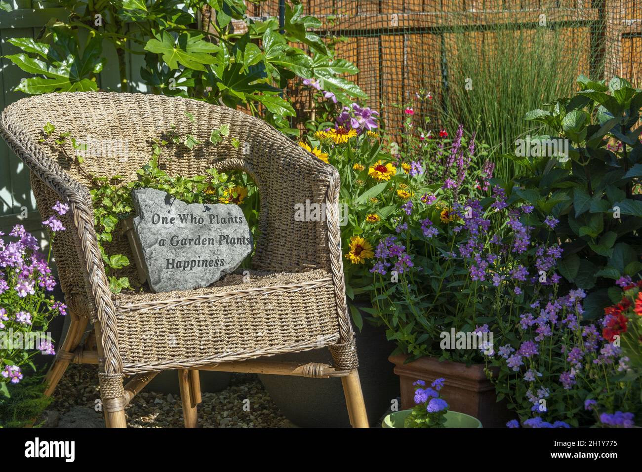 Chaise en osier surcultivée dans un petit jardin avec plaque de pierre lisant « un jardin qui plante des plantes du bonheur » Banque D'Images