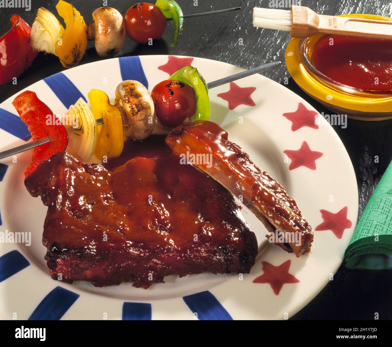 Barbecue de côtes de rechange avec sauce et brochette de légumes rôtis poivron rouge tomate sur étoile et plaque de rayures sur ardoise brillante avec sauce rouge et brosse à badigeonner Banque D'Images