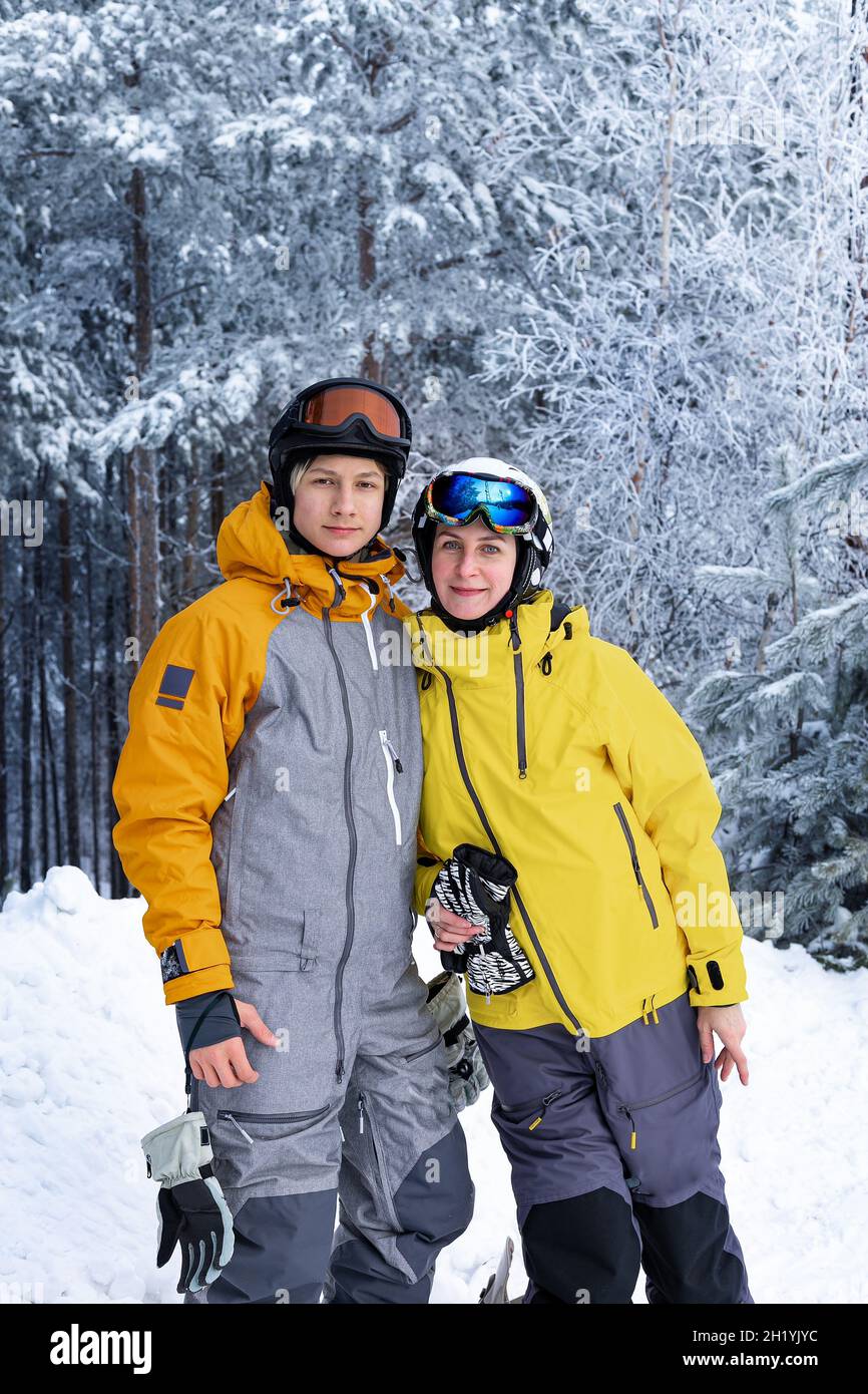 Portrait d'hiver de personnes heureuses d'origine caucasienne dans des casques et des lunettes de ski.Femme et son fils sur fond de forêt enneigée.Famille Banque D'Images