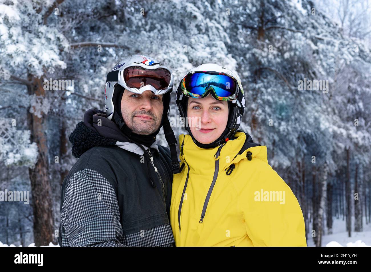 Portrait d'un homme et d'une femme d'origine caucasienne dans des casques et des lunettes de ski sur fond de forêt enneigée.Des vêtements de couleurs vives pour une vie active Banque D'Images