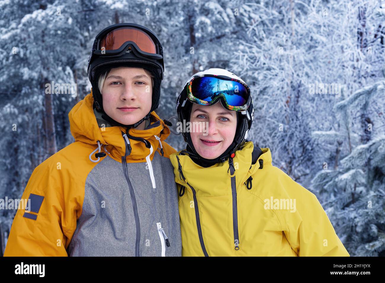 Portrait d'hiver de personnes heureuses d'origine caucasienne dans des casques et des lunettes de ski.Femme et son fils sur fond de forêt enneigée.Famille Banque D'Images