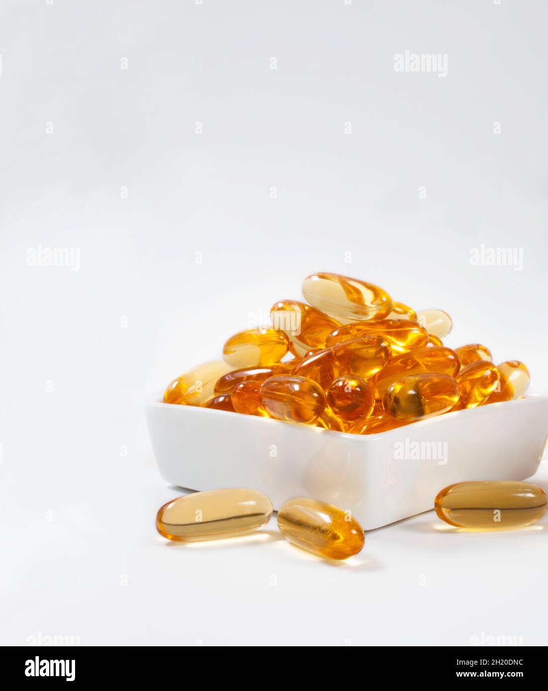 Capsules d'huile de poisson dans un bol en porcelaine sur fond blanc Banque D'Images