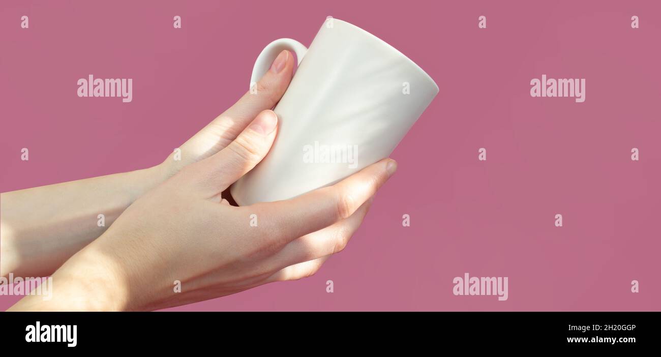 mains de femmes tenant une tasse blanche sur fond rose.Concept de boissons alimentaires.Copier l'espace. Banque D'Images