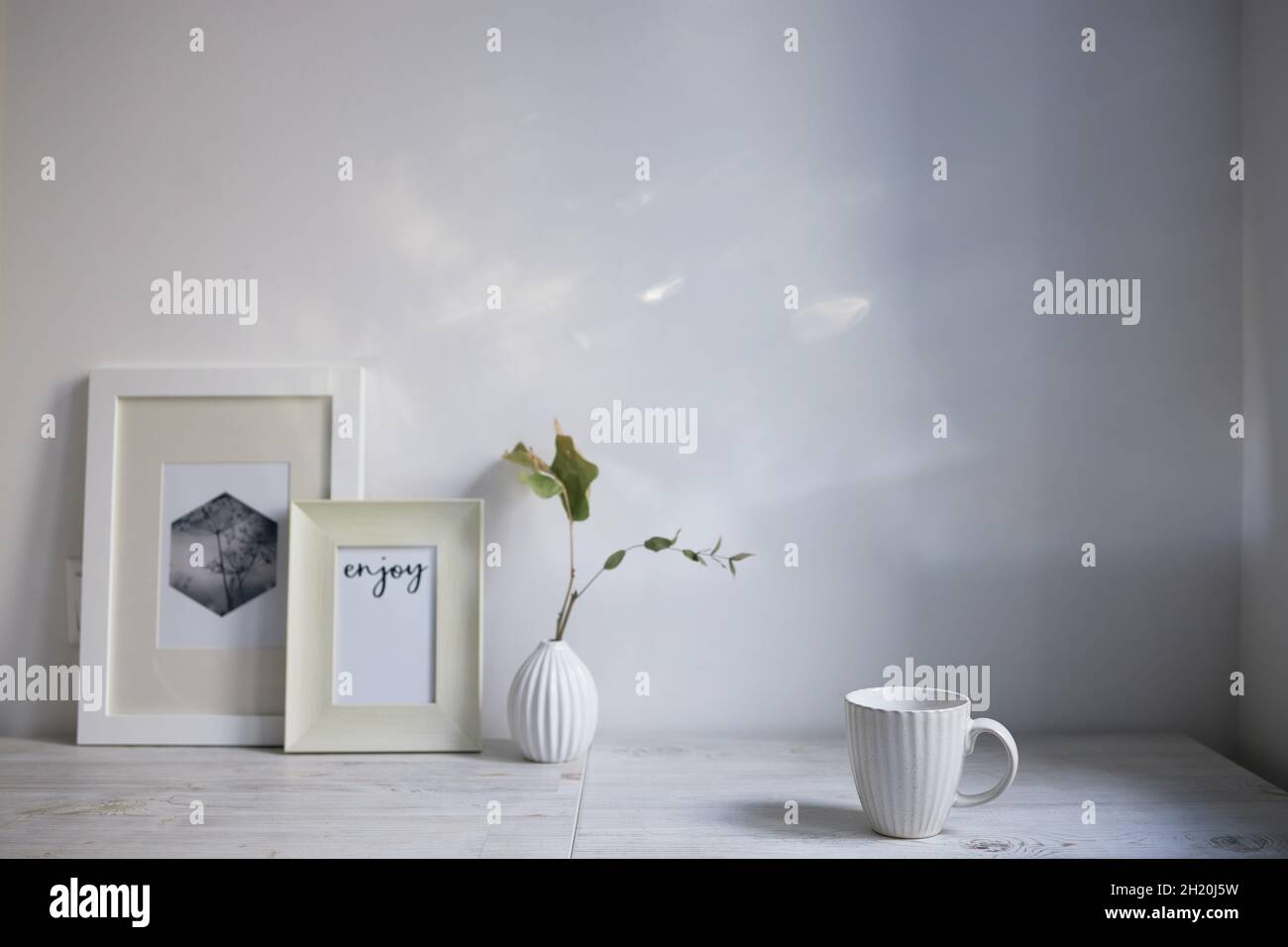 Style scandinave. Design intérieur. Une tasse blanche, un petit vase avec une branche d'eucalyptus séché, deux cadres photo sont sur la table. Copier l'espace pour tex Banque D'Images