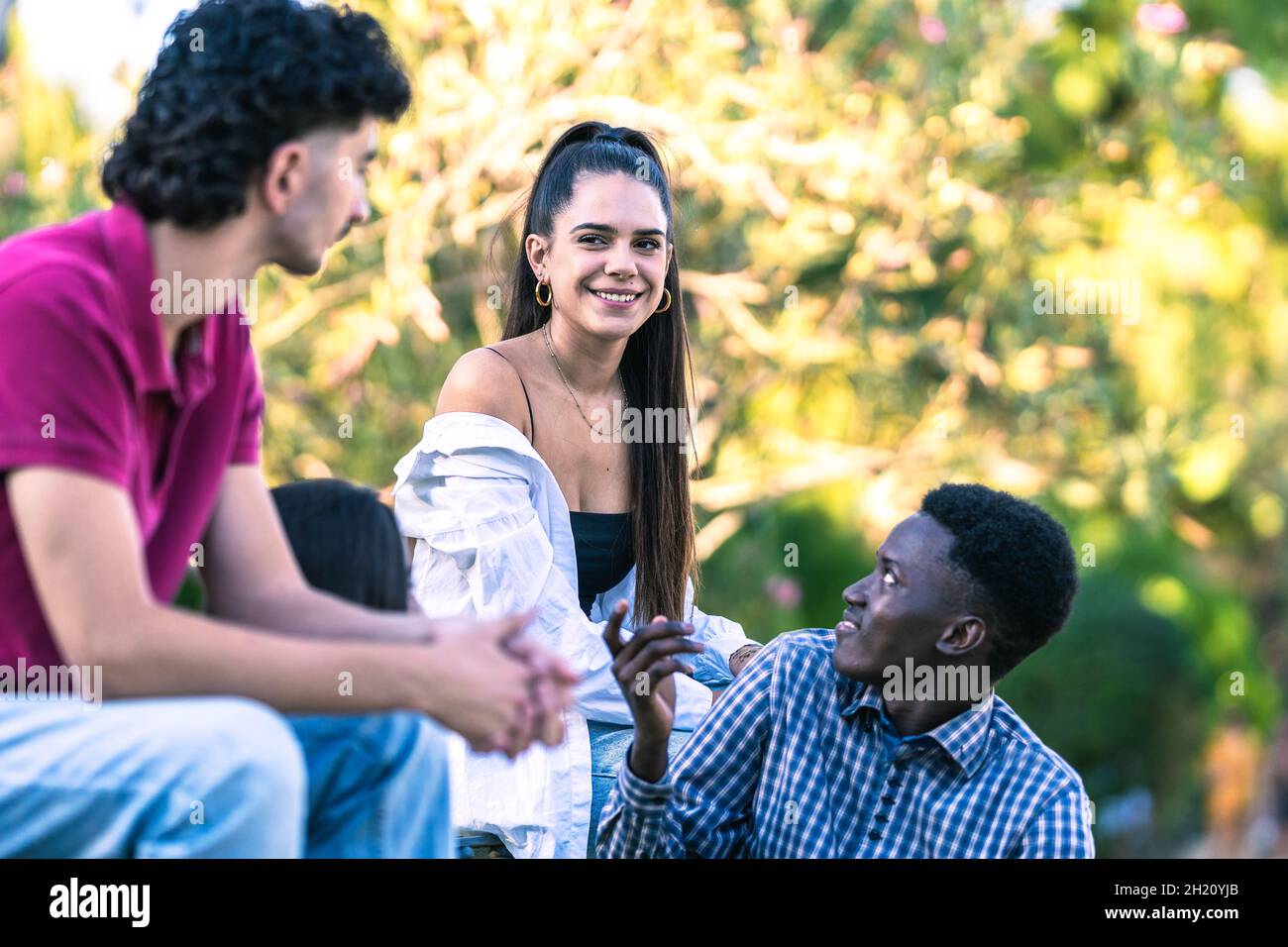 Divers jeunes assis sur un banc dans le parc tout en parlant en été Banque D'Images