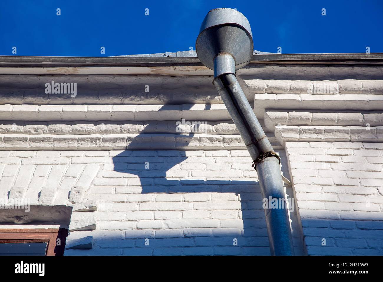 une gouttière d'un tuyau de pluie galvanisé à l'avant-pied d'un bâtiment avec une façade blanche en briques blanches par temps clair ensoleillé. Banque D'Images