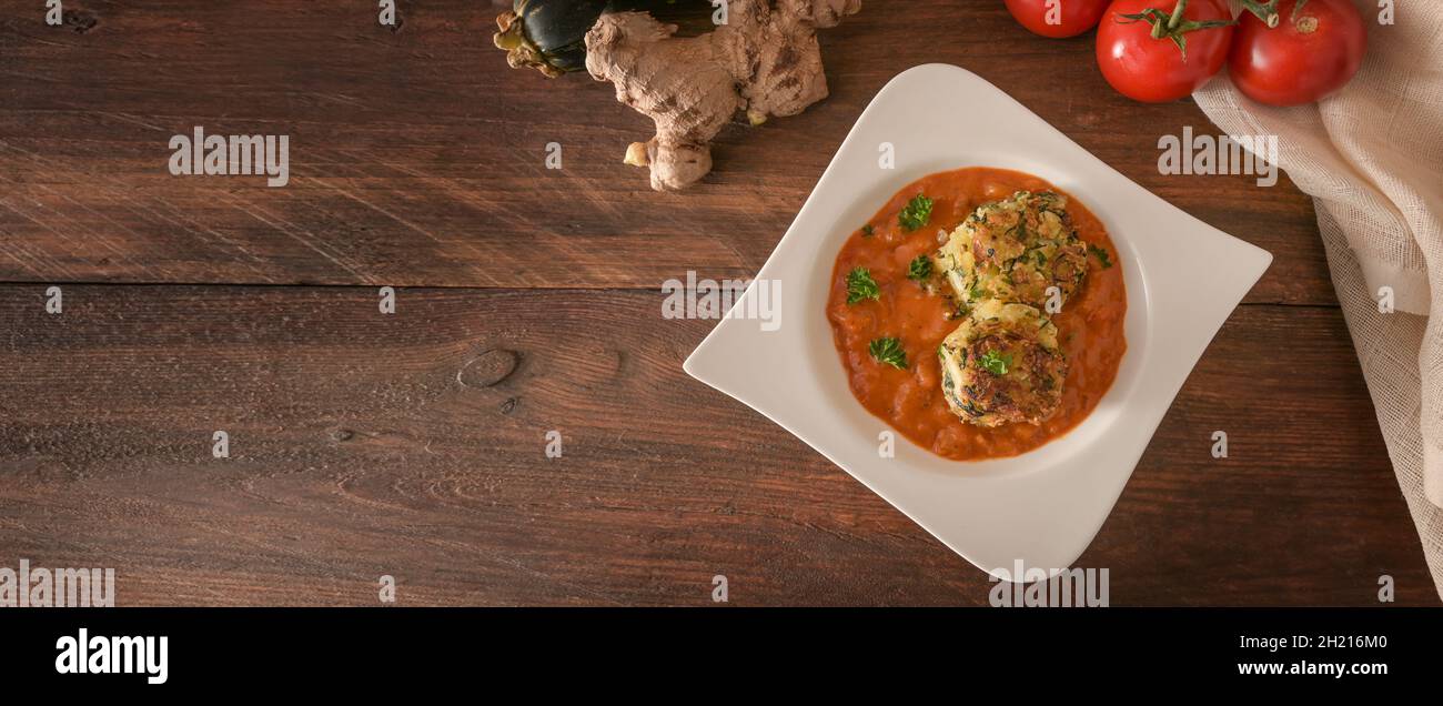 Crème de tomate avec boulettes de légumes frites dans une assiette blanche et quelques ingrédients sur des planches de bois rustiques sombres, format panoramique, espace de copie, grand angle v Banque D'Images