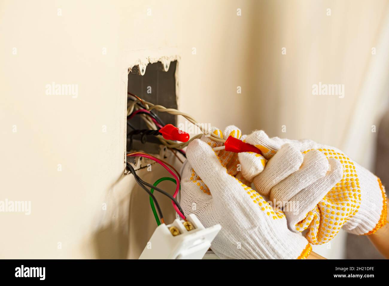 Un électricien remplace un interrupteur mural.Un concept de projet DIY.Danger de haute tension.Les gants professionnels résistants aux chocs se serrent sans fil Banque D'Images