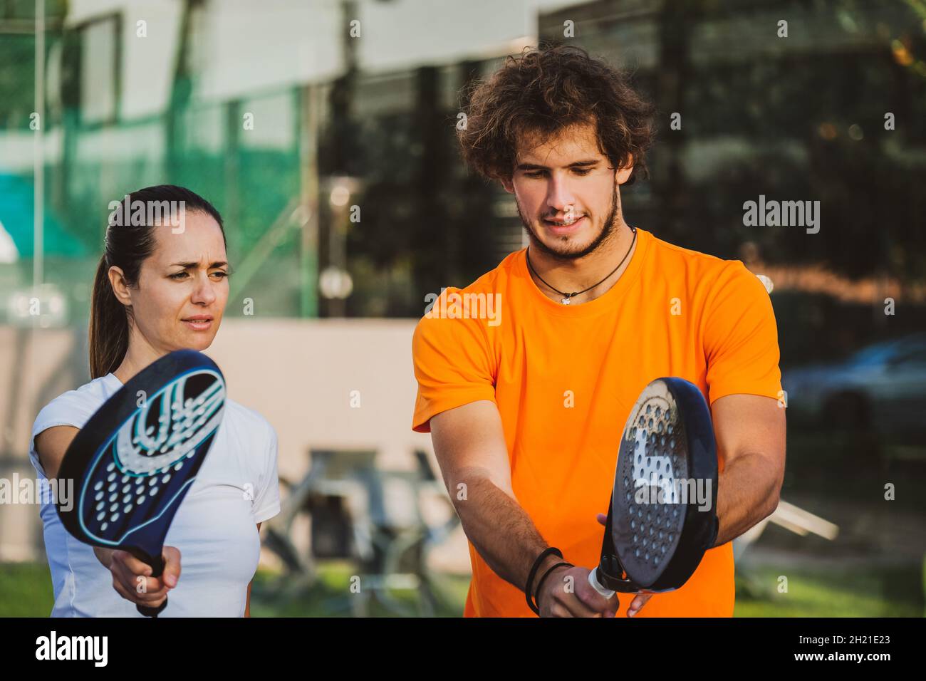 Un jeune enseignant suit la leçon de padel à son étudiant - l'entraîneur enseigne à la fille comment jouer padel sur le court de tennis extérieur Banque D'Images