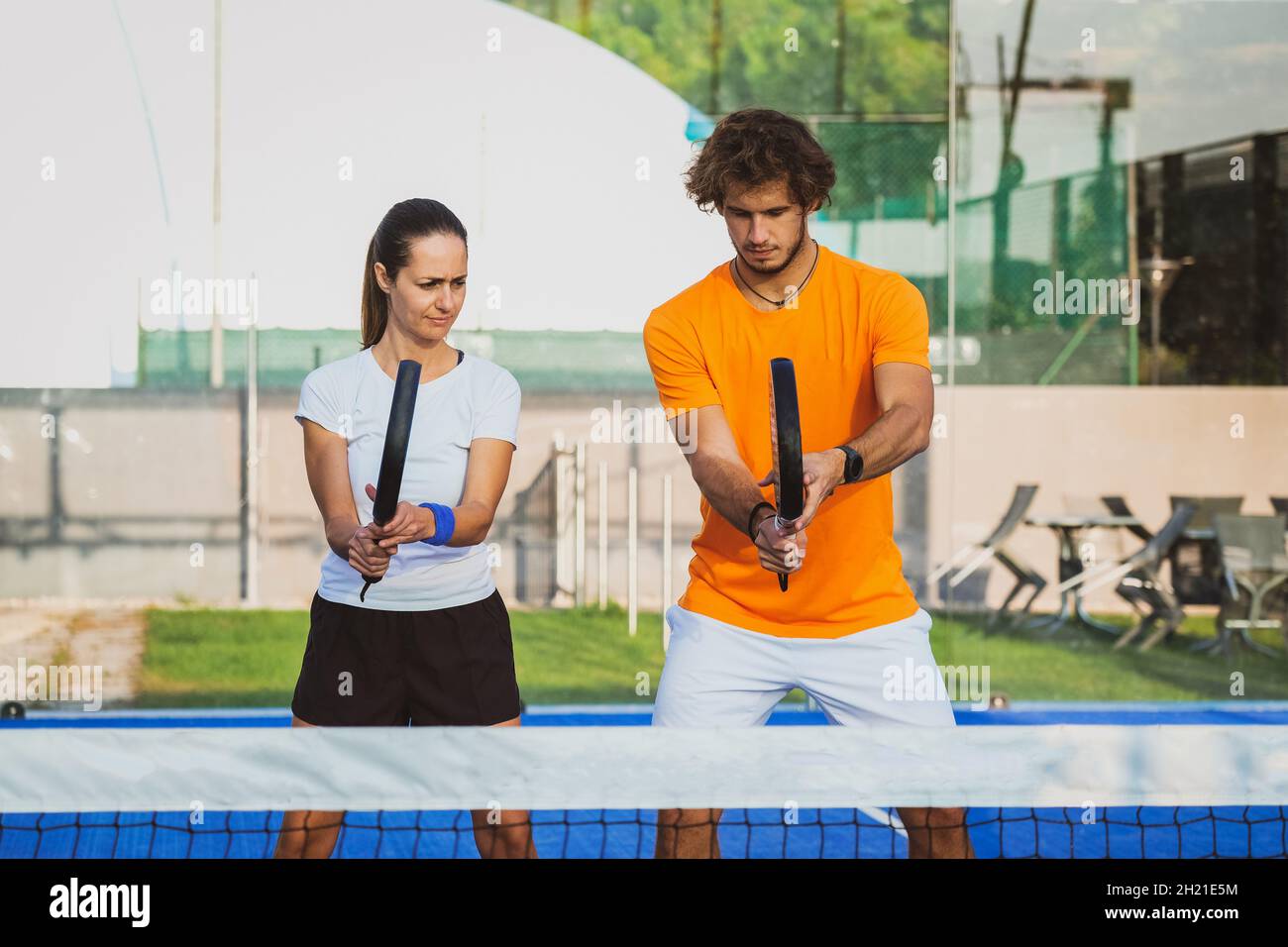 Un jeune enseignant suit la leçon de padel à son étudiant - l'entraîneur enseigne à la fille comment jouer padel sur le court de tennis extérieur Banque D'Images