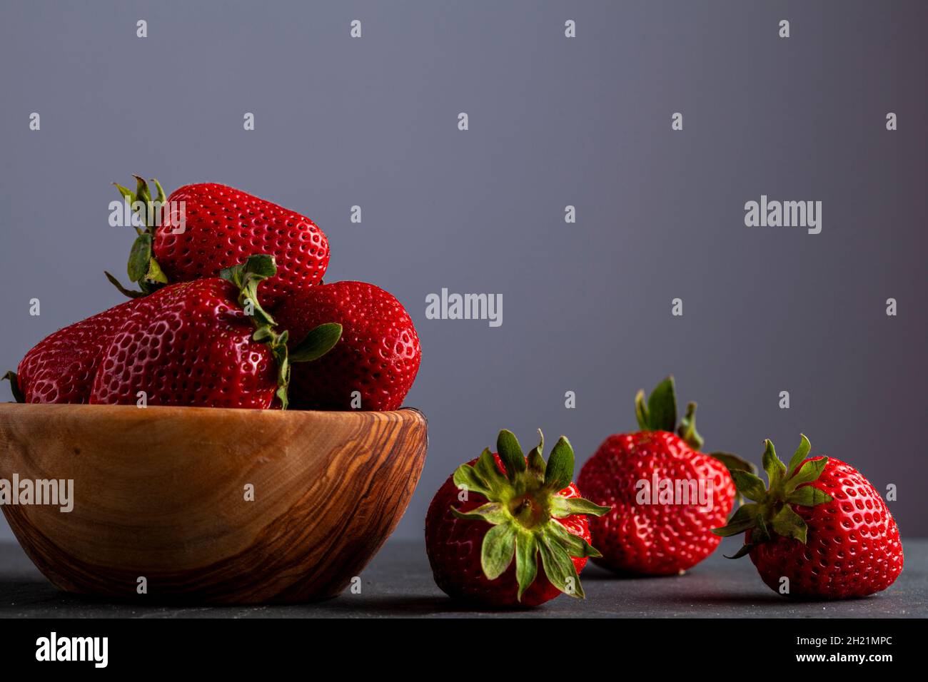 Gros plan image isolée d'un bol en bois rempli de fraises fraîches crues sur fond de pierre sombre.Riche en nutriments, nourriture biologique brute pour lui Banque D'Images