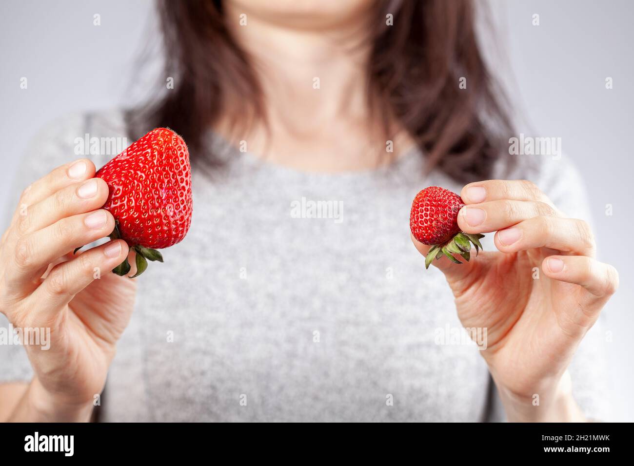 Une femme blanche tient une grosse et une petite fraise dans sa main.Image de concept pour les pratiques agricoles naturelles et les méthodes hybrides de sp. Induites par les hormones de croissance Banque D'Images