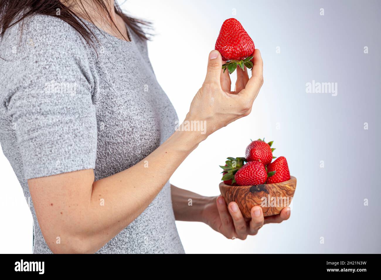 La jeune femme caucasienne portant un t-shirt à manches courtes mange un en-cas de fraise.Vue latérale photo montre elle tenant un bol en bois de baies.Été, hein Banque D'Images