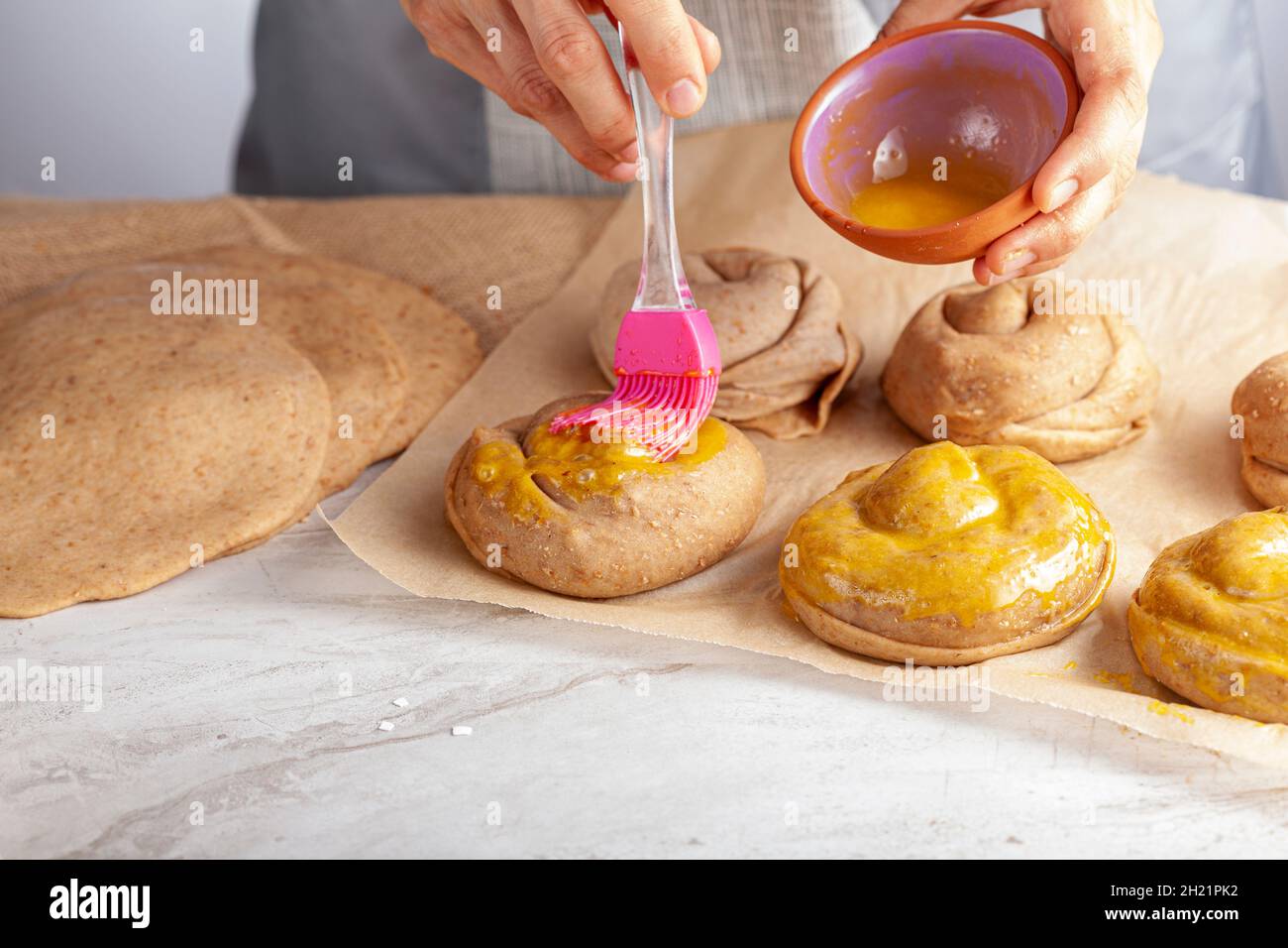 gros plan image isolée d'une femme caucasienne préparant des petits pains de pâtisserie turque avec du tahini et du pétimezi.Elle étend le jaune d'œuf sur le dessus en utilisant le slicon br Banque D'Images