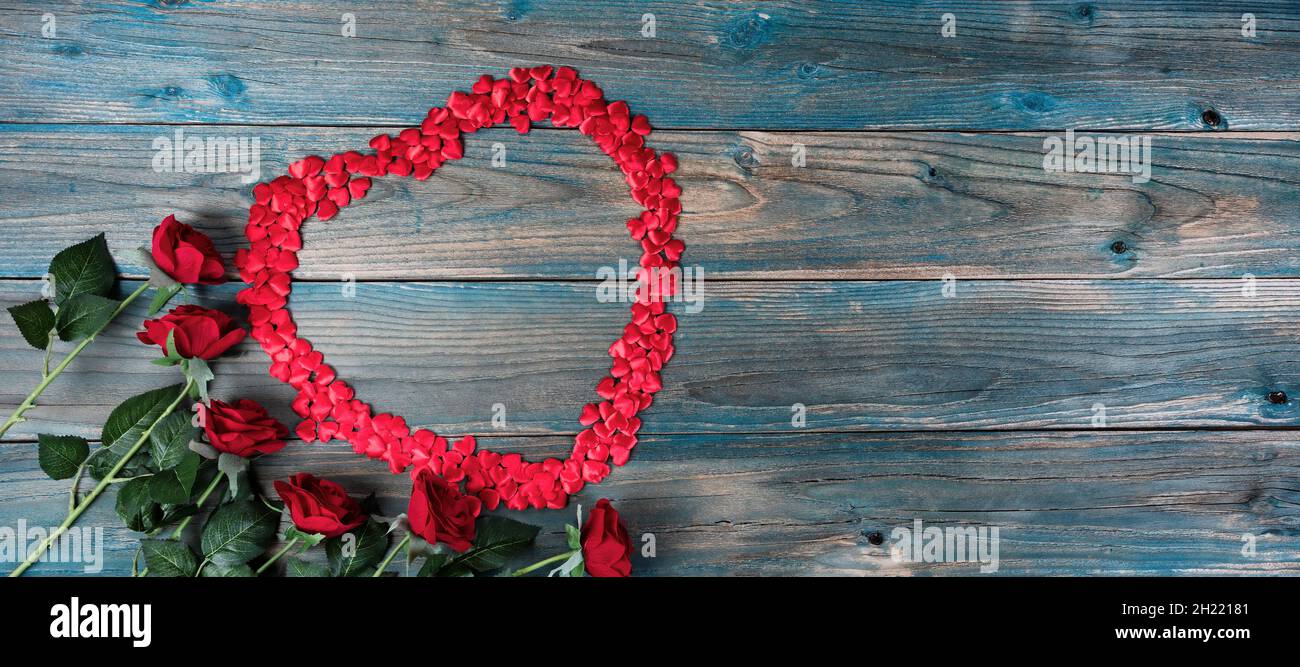 Saint-Valentin arrière-plan de vacances avec roses rouges et petites formes de coeur formant grand coeur contour sur des planches de bois bleu pâle Banque D'Images