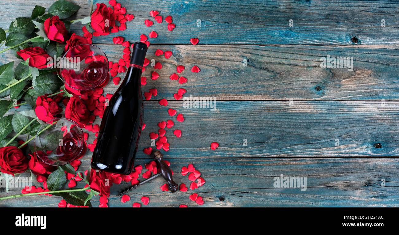 Vacances de Saint-Valentin avec une bouteille de vin, des verres à boire, des roses rouges, un ouvre-tire-bouchon et de petites formes de coeur sur le bleu pâle en bois pl Banque D'Images