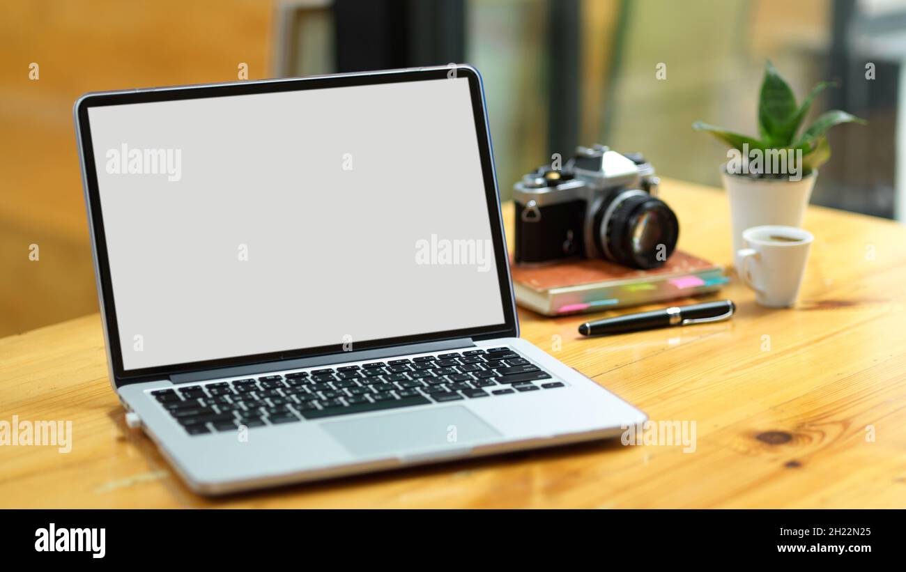 Gros plan, support d'ordinateur portable moderne ouvert sur la table de travail avec appareil photo et fournitures vintage. Banque D'Images