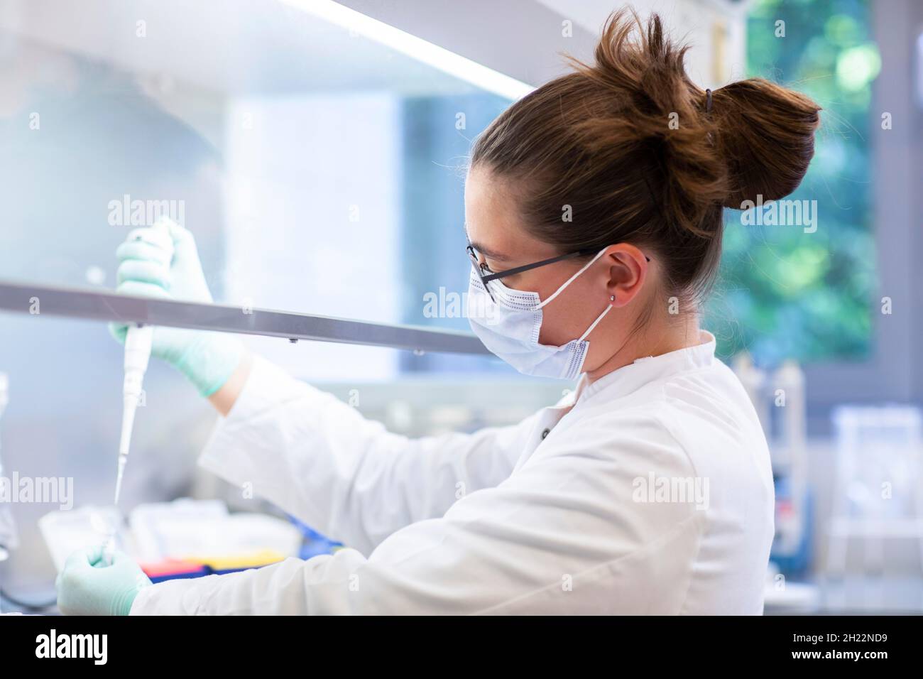 Un jeune technicien de laboratoire portant un masque facial et pipetant un échantillon dans un laboratoire équipé d'un équipement de laboratoire dans un flux de travail, Fribourg Banque D'Images