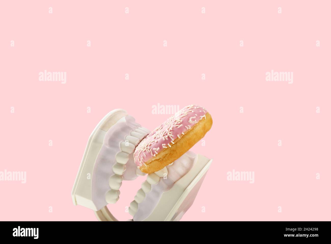 Les mâchoires en plastique maintiennent le donut rose doux dans les dents.Concept de santé dentaire, dentisterie et caries. Banque D'Images