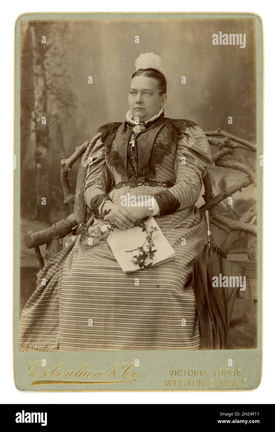 Femme victorienne 1890 ans Carte victorienne originale du cabinet de riches bien à faire, riche classe moyenne prospère, femme chrétienne religieuse mature, regardant sérieuse, sévère, probablement catholique, portant une robe élaborée avec jambe de manches mouton, chapeau de dentelle, crucifix exposé montrant qu'elle est pieuse, un parapluie à ses côtés, tenant un journal pour montrer qu'elle est éduquée, du studio de Debenham & Co., Victorian Lodge, Western-Super-Mare, Somerset, Angleterre, Royaume-Uni daté de juin 1894 Banque D'Images