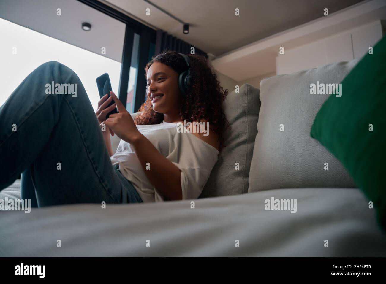 Femme pluriethnique se détendant au lit sourire, en écoutant de la musique et en envoyant des SMS Banque D'Images
