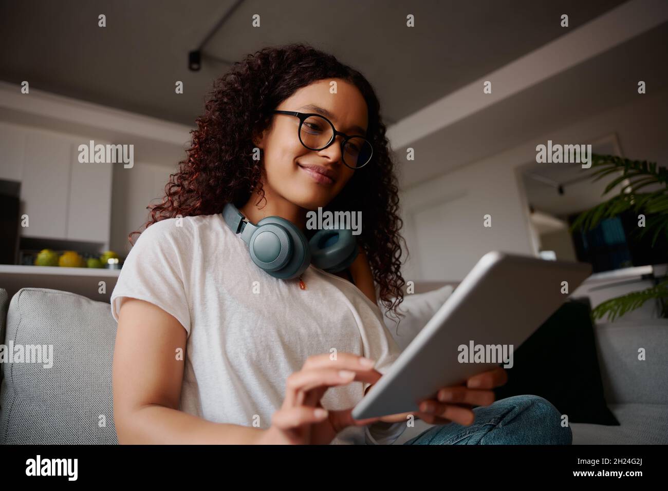 Jeune femme adulte multiethnique souriant tout en utilisant une tablette.Faible angle sur le canapé Banque D'Images