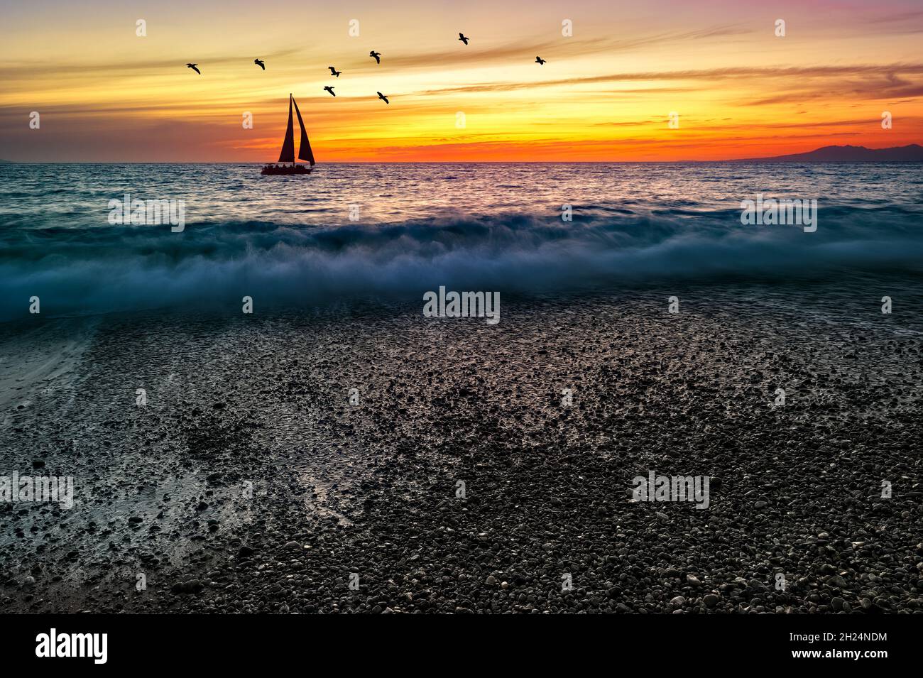 Un voilier navigue le long de l'océan contre Un ciel coloré de coucher de soleil avec oiseaux volant au-dessus de la tête Banque D'Images
