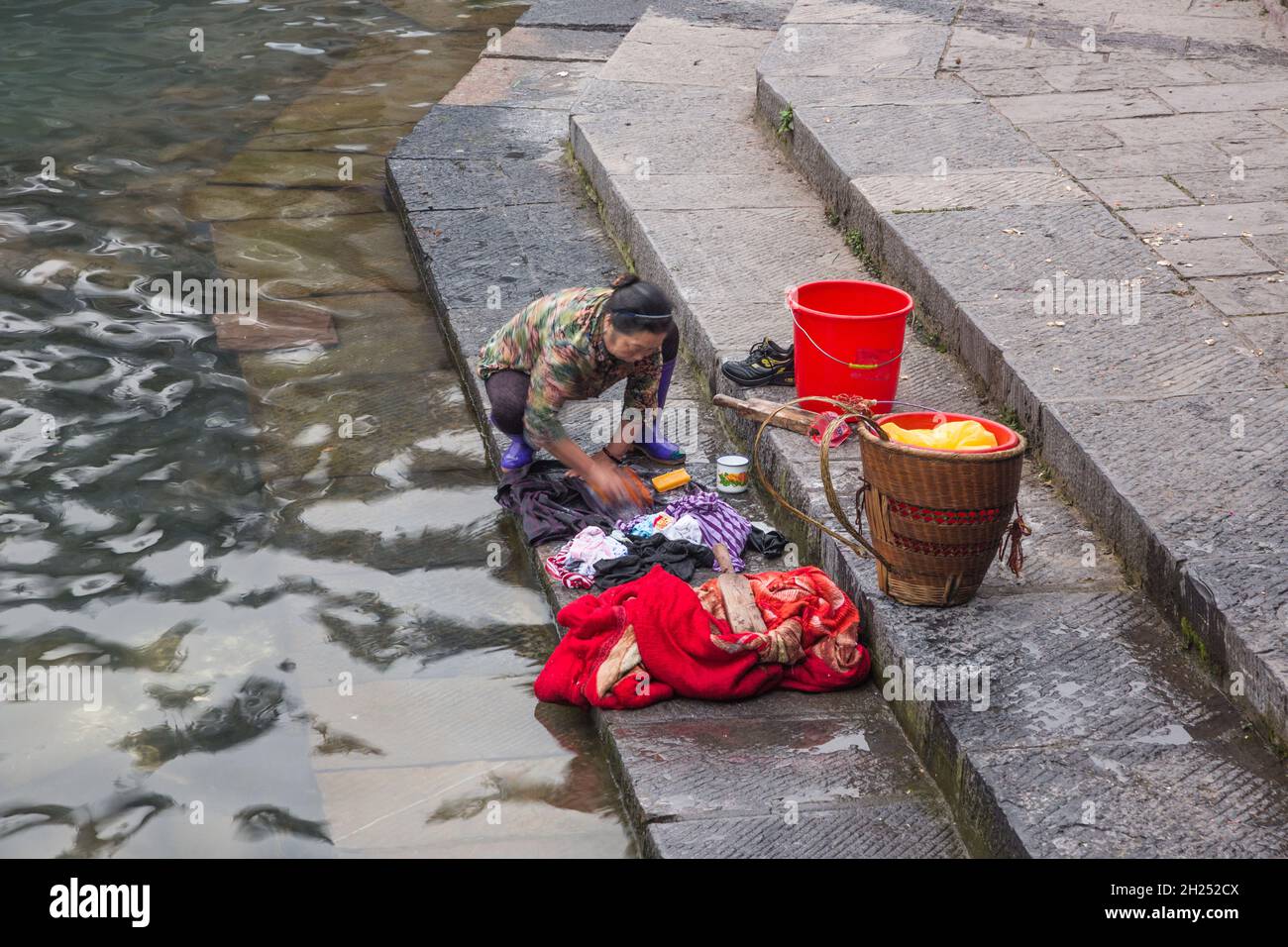 Une femme chinoise lave la lessive à la main sur les marches de la rivière Tuojiang à Fenghuang, en Chine. Banque D'Images