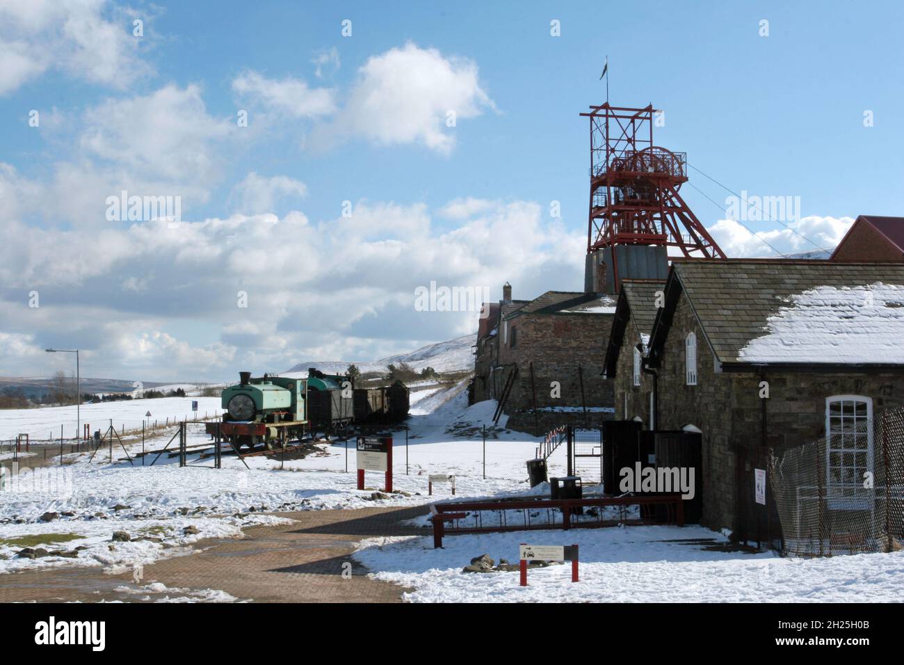 Big Pit, musée de l'exploitation minière, train à vapeur et wagons enroulement bâtiments engrenage bleu ciel bleu ciel blanc moelleux nuages hiver neige Blaenafon Wales UK Copy space Banque D'Images