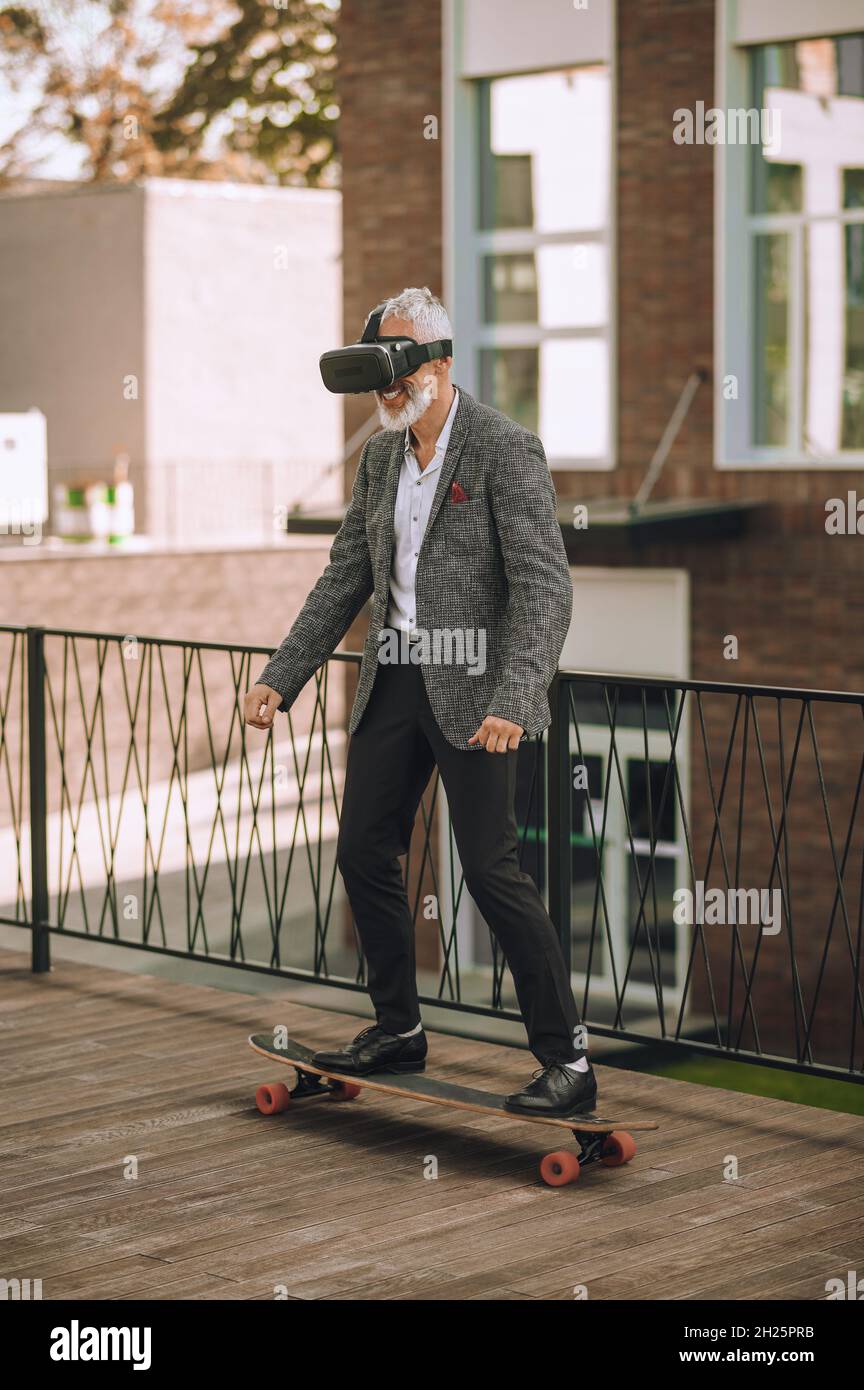 Skateboarder excité dans des lunettes VR s'amusant à l'extérieur Banque D'Images