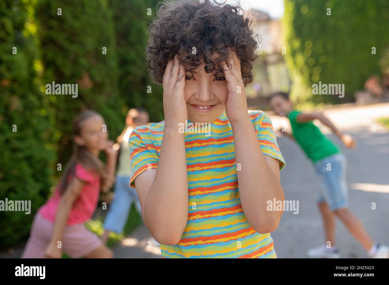 Garçon souriant couvrant le visage avec des palmiers et se cachant des amis Banque D'Images